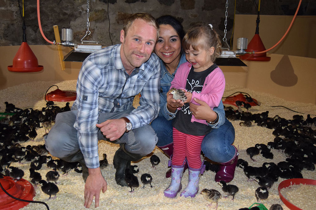 Michie family crouching among many chicks, with their daughter holding a chick.