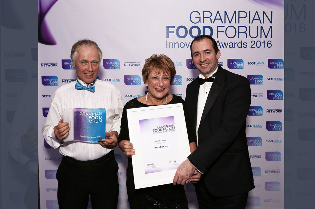 Three people at an awards event holding a certificate in front of a Grampian Food Forum backdrop.