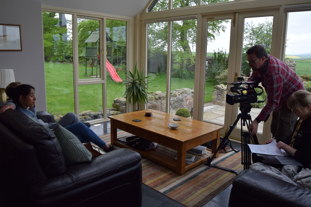Interior scene with camera equipment, a person on a sofa, and a view to a green garden.