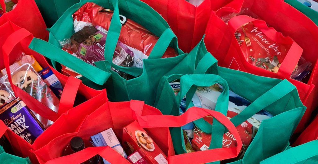 Xmas Food Shop Multiple red and green shopping bags filled with assorted groceries and snacks.