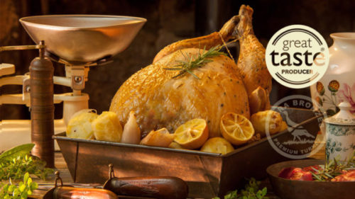 Roasted turkey with herbs on a table with lemons, potatoes, and antique kitchen scale.